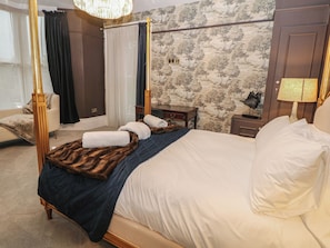 Ein Bett mit Baldachin, ausgestattet mit einem Fellüberwurf, ein Holznachttisch, eine Lampe und eine Wand mit Baumdekor.
