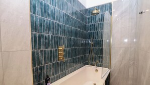 Moderni kylpyhuone, jossa on erillinen kylpyamme, suihkupää ja shampoopullo ammeen reunalla.