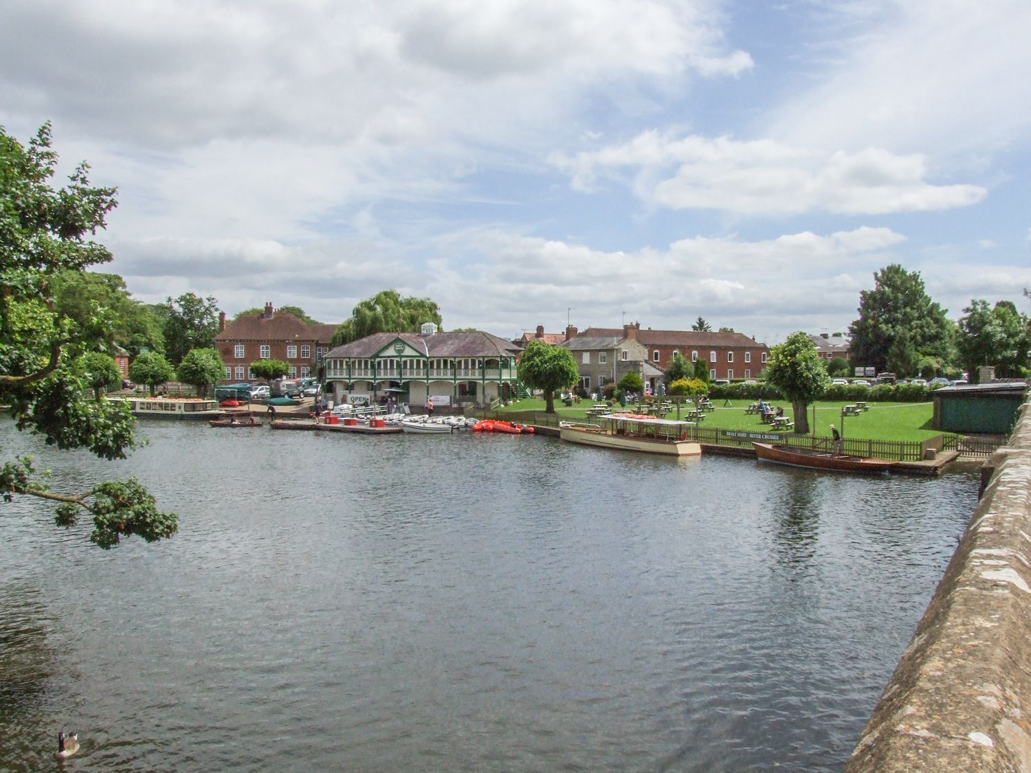 A riverside view with a dock, boats, and a green building with a sign that says 'OPEN'.