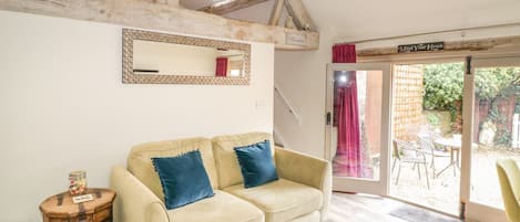 Una habitación acogedora con sofá, un barril de madera, un espejo y una puerta que da a un espacio exterior.