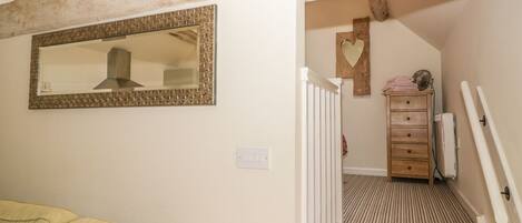 A staircase with a striped carpet, a wooden dresser with a heart-shaped mirror, and a sign above the stairs.