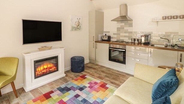 A living room with a fireplace, a television, a kitchen with a stove, and a couch. - The Bolt Hole (Stratford-upon-Avon)