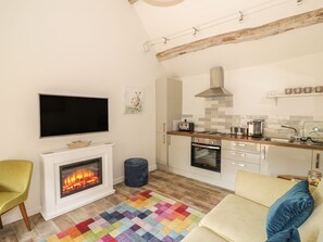 Ein Wohnzimmer mit Kamin, Fernseher, einer Küche mit Herd und einer Couch.