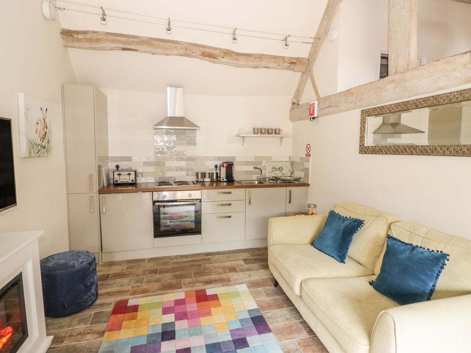 A cozy living room with a sofa, a fireplace, and a kitchen area with a tiled backsplash and wooden beams.