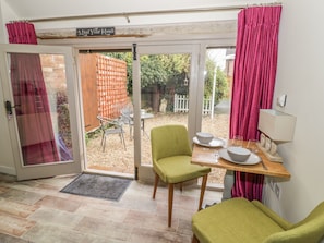 A room with a dining table set for two, a green chair, a wooden bench, and a small table with a lamp. - The Bolt Hole (Stratford-upon-Avon)