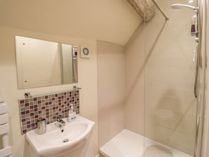 A bathroom with a glass-enclosed shower, a white sink, a mirror, and a tiled backsplash. - The Bolt Hole (Stratford-upon-Avon)