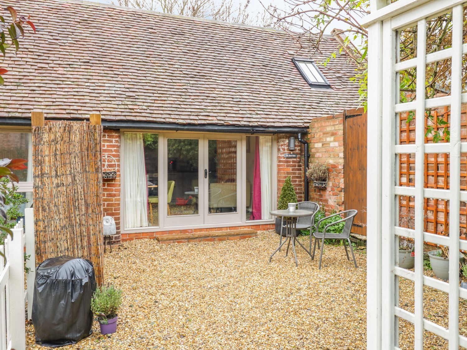 A brick house with a tiled roof, a covered patio area with gravel, and a white fence.