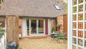 A brick house with a tiled roof, a covered patio area with gravel, and a white fence. - The Bolt Hole (Stratford-upon-Avon)