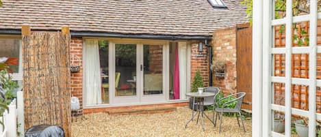 A brick house with a tiled roof, a covered patio area with gravel, and a white fence.