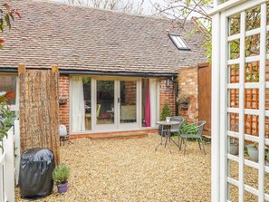 A brick house with a tiled roof, a covered patio area with gravel, and a white fence. - The Bolt Hole (Stratford-upon-Avon)