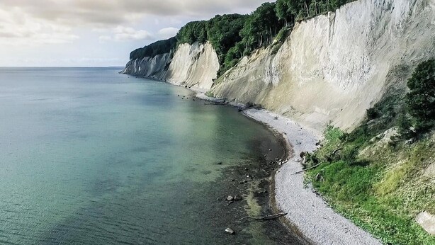 A coastal landscape with cliffs, clear water, and a narrow beach.