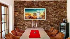A dining area with a stone wall, a framed landscape painting, a candelabra, and leather chairs.