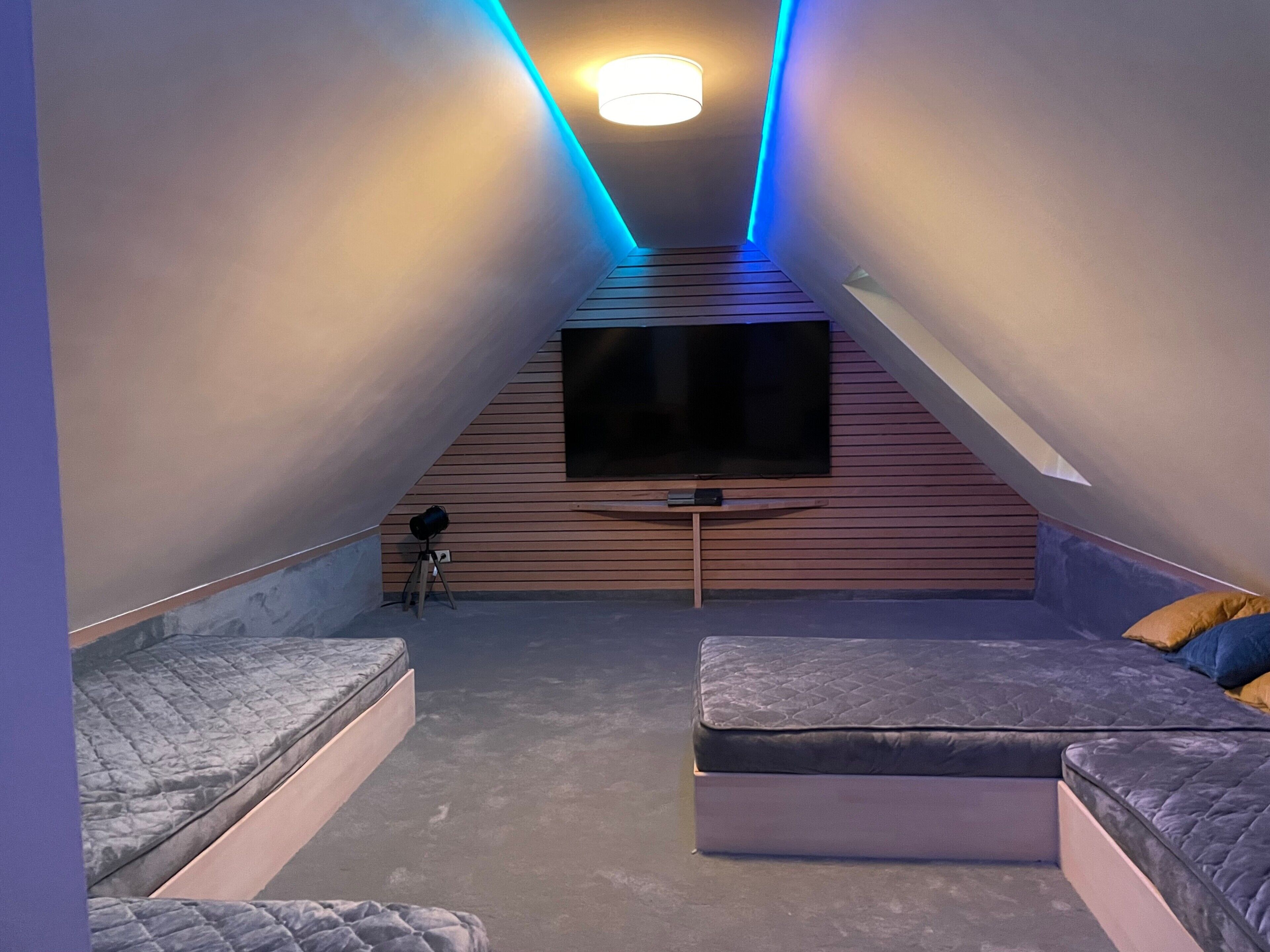 Una habitación con techo inclinado, un televisor de pantalla plana en la pared, un telescopio sobre trípode y dos sofás.