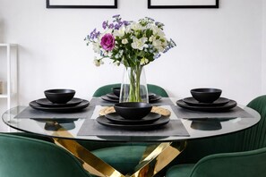 Een ronde eettafel met zwarte kommen en borden, een bloevas en groene stoelen.