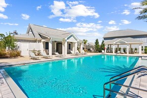 A swimming pool with lounge chairs, a covered patio, and a building with a gabled roof. - Stay where Serenity Meets Luxury (Panama City Beach)