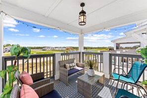 A covered outdoor seating area with wicker furniture, a potted plant, and string lights. - Stay where Serenity Meets Luxury (Panama City Beach)
