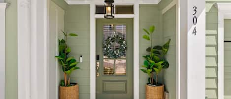 A green door with a welcome mat, two potted plants, and a number '304' on the wall.