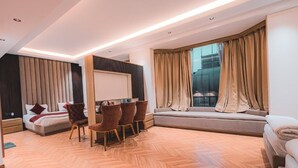 Quarto de hotel moderno com cama, escrivaninha, cadeiras, sofá e uma grande janela com cortinas.