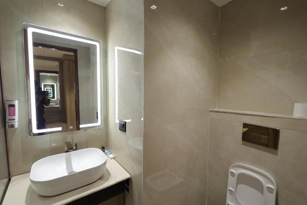 A modern bathroom with a large oval sink, a mirror with integrated lighting, a toilet, and a shower area.