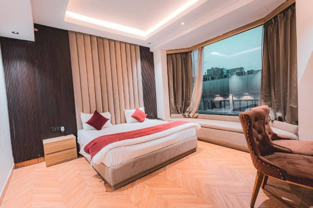 A modern hotel room with a large bed, a window with a city view, a wooden floor, and a brown leather chair.