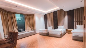Una habitación de hotel moderna con suelo de espiga, un sofá, dos camas y ventanas grandes con cortinas.
