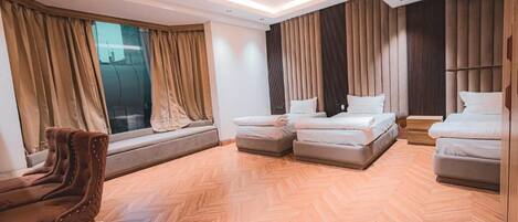 A modern hotel room with a herringbone floor, a sofa, two beds, and large windows with curtains.
