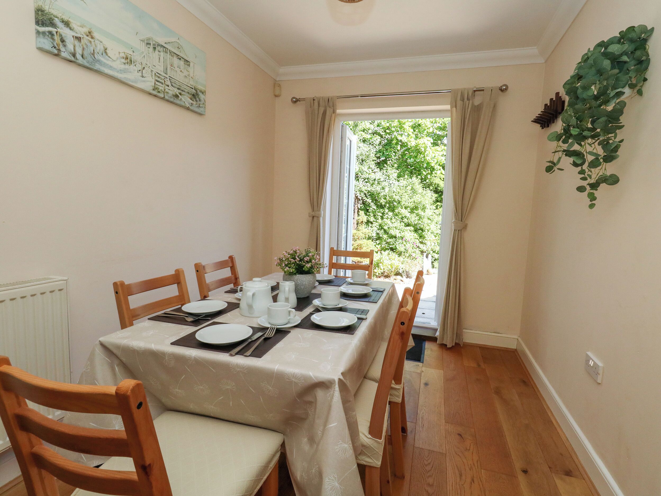 A dining room with a table set for four, wooden chairs, a radiator, a window with curtains, and a painting on the wall.