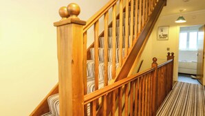 Un escalier en bois avec une moquette à rayures, une main courante en bois et un tableau accroché au mur.