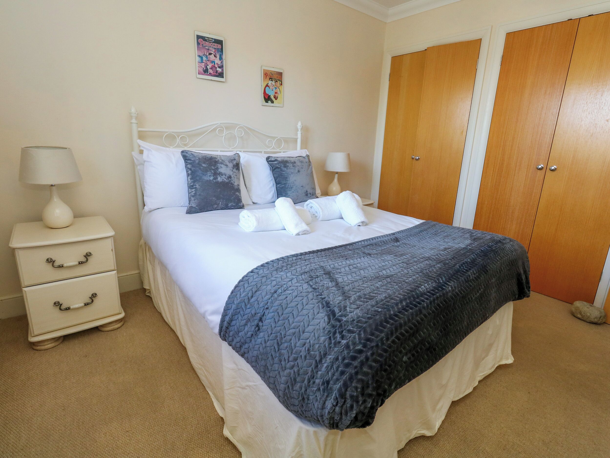 A neatly made bed with pillows, a bedside table with a lamp, and a wardrobe.