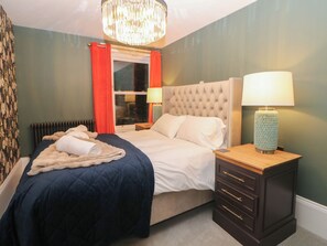 A neatly made bed with a duvet, a bedside lamp, and a nightstand with drawers. - The Devonshire Suite (Buxton)
