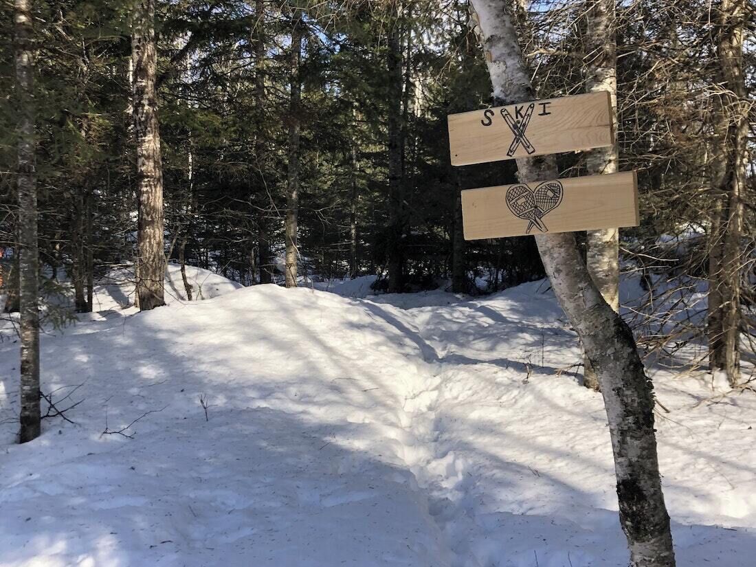 A wooden signpost with ski and heart symbols in a snowy forest.