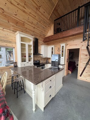 A kitchen with wooden paneling, a granite countertop, white cabinetry, and a black stove.