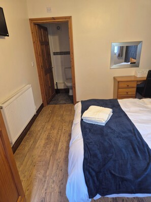 Ein Schlafzimmer mit einem Bett, einer hölzernen Kommode, einem Spiegel und einer Tür zu einem Badezimmer.