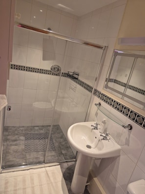 Ein Badezimmer mit einer Duschkabine, einem Standwaschbecken und einem Spiegel darüber.