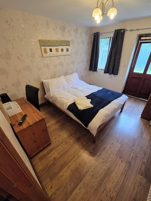 Ein Schlafzimmer mit Bett, Schreibtisch, Stuhl, Vorhängen und einer Tür.