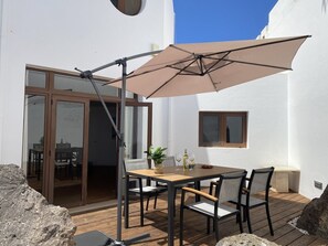 Eine Terrasse mit Tisch und Stühlen, einem großen Sonnenschirm und Blick ins Innere.
