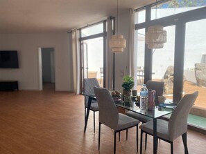 Ein Essbereich mit einem Glastisch, vier Stühlen, einer Pflanze und einer Wasserflasche.