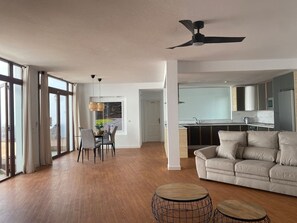 Ein geräumiger Wohnbereich mit Sofa, Esstisch und einer Küche im Hintergrund.