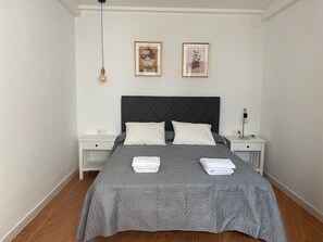 Ein Schlafzimmer mit einem Bett, zwei Nachttischen, einer Hängelampe und zwei gerahmten Bildern an der Wand.