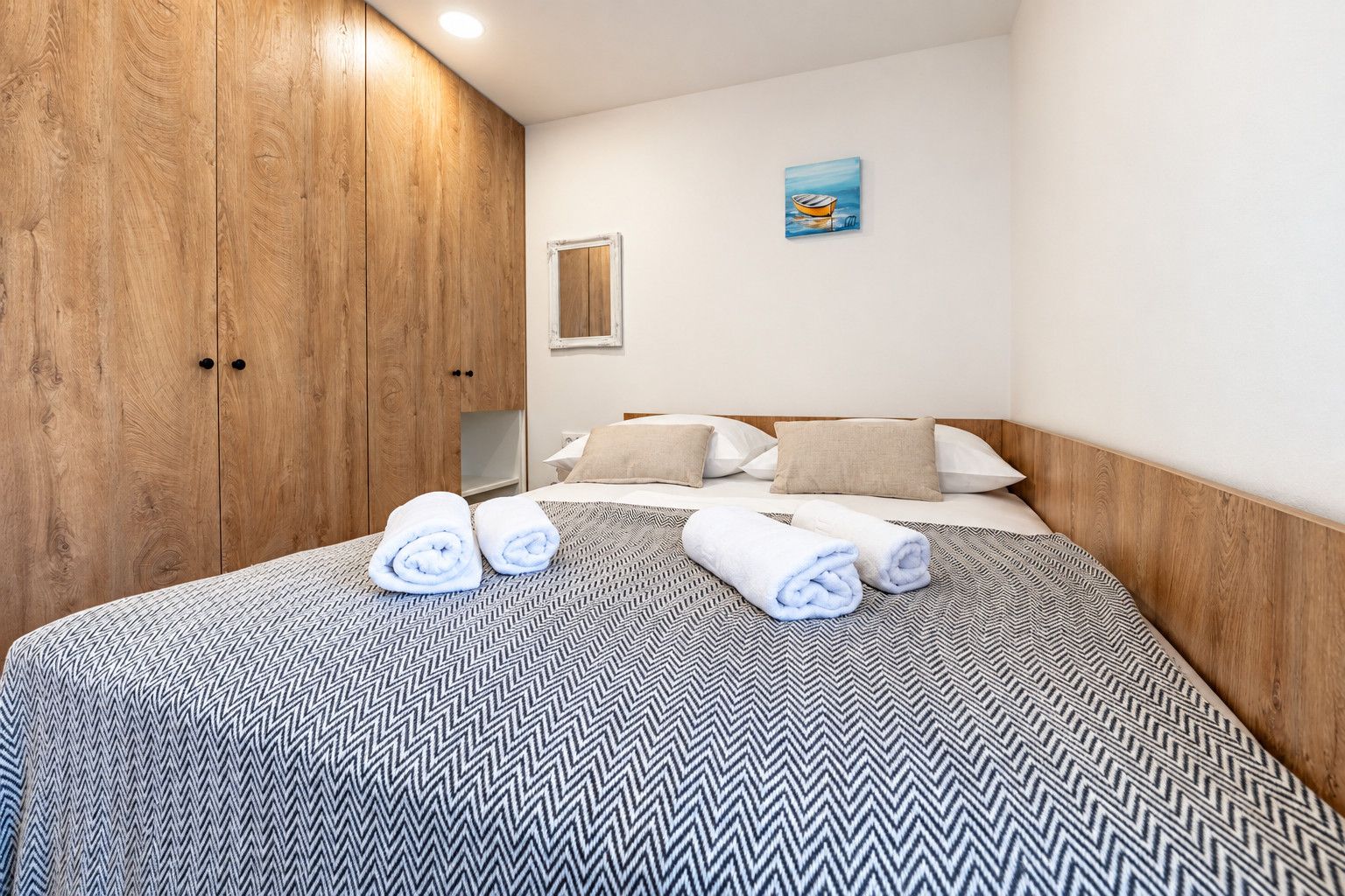 A hotel room with a bed, wooden wardrobe, and a painting on the wall.