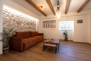 Una sala de estar acogedora con pared de piedra, vigas de madera, un sofá marrón, una mesa de centro de madera y un cuadro con gaviotas.