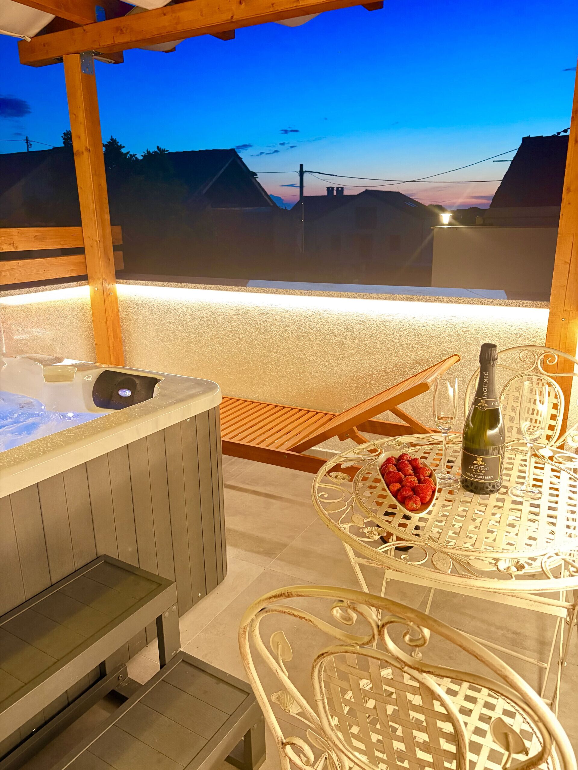 A hot tub, a table with a bottle of champagne, and a bowl of strawberries.