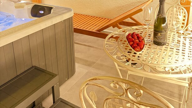 Uma banheira de hidromassagem, uma mesa com uma garrafa de champanhe e uma taça de morangos.