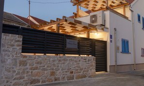 Eine Steinsäule mit einem Metallgitter, einer Holzpergola und einem Schild, das ein Ferienhaus kennzeichnet.