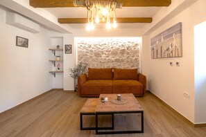 Een woonkamer met een bank, een salontafel, een stenen muur en een schilderij.