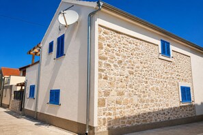 Un edificio con fachada de piedra, contraventanas azules y una antena parabólica.