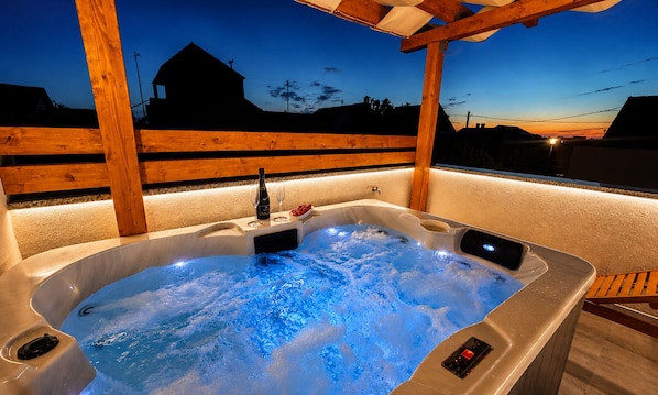 Een jacuzzi met een houten terras en een uitzicht op huizen in de verte.