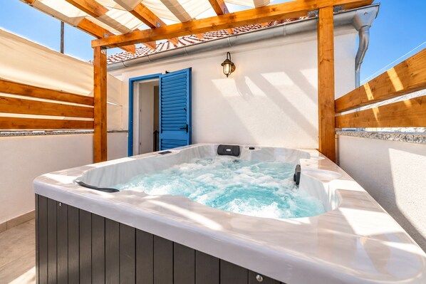 Un jacuzzi bajo una pérgola de madera con una puerta azul y una lámpara de pared.