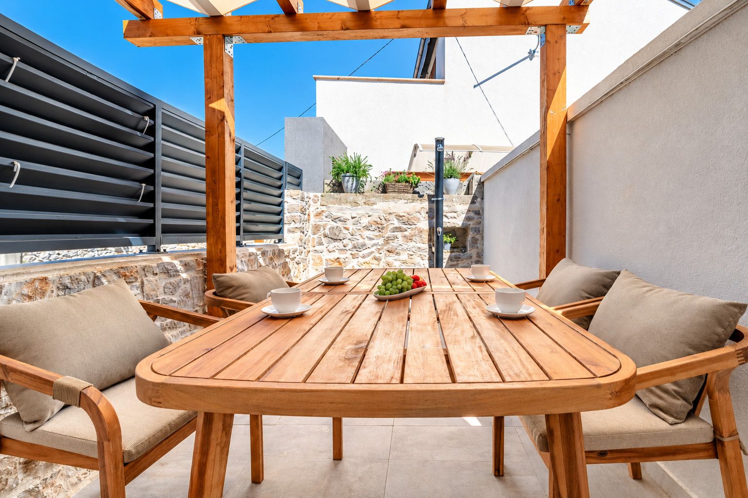 Un espace extérieur aménagé avec des meubles en bois, comprenant une table et des chaises, un mur en pierre et une vue sur un bâtiment en arrière-plan.