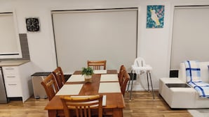 Uma área de refeições com mesa e cadeiras de madeira, um sofá branco, uma cadeira branca e um relógio na parede.